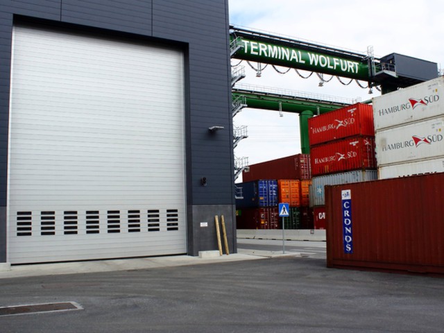 A large EFAFLEX high speed door closed at a container terminal, alongside the terminal gantry crane and stacked shipping containers