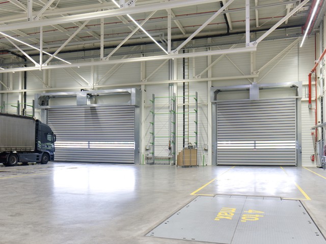 Two large EFAFLEX high speed doors closed side by side in a warehouse hall, with a curtain sided lorry parked inside alongside the left hand door
