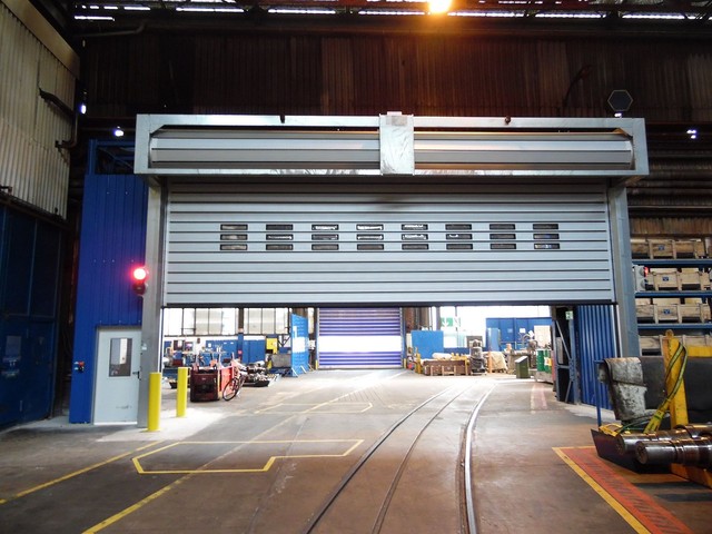 Machinery is visible beyond a large EFAFLEX high speed door raised part way, with vision windows across the leaf and rail tracks running through the opening