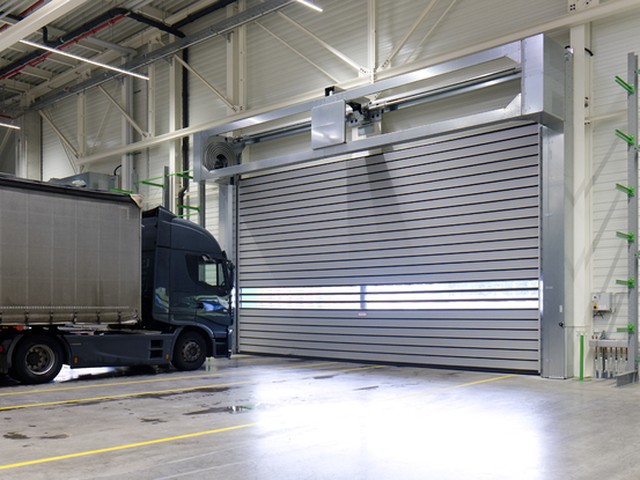 An EFAFLEX high speed spiral door closed across a wide hall opening, its coiled leaf showing in the open headgear above and a curtain sided lorry alongside