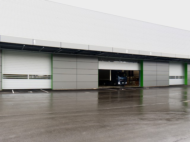 Three numbered loading bays with white EFAFLEX high speed doors run along a clad building, the middle door part raised with a lorry inside